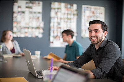 A young male student smiles as he does group work with a peer