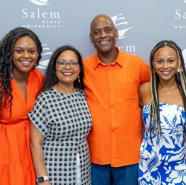 Nate Bryant, his wife and two daughters pose for a photo in front of a Salem State backdrop at his retirement celebration.