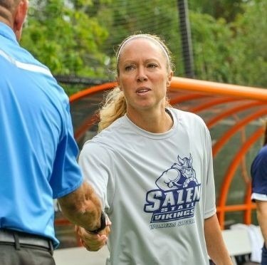 Director of Athletics Nicky Wood wearing a gray Vikings shirt reaches out to shake a hand after a game.