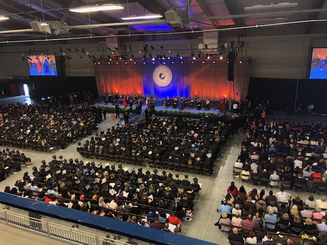 Graduates and guests seated at commencement ceremony; view from the bleachers