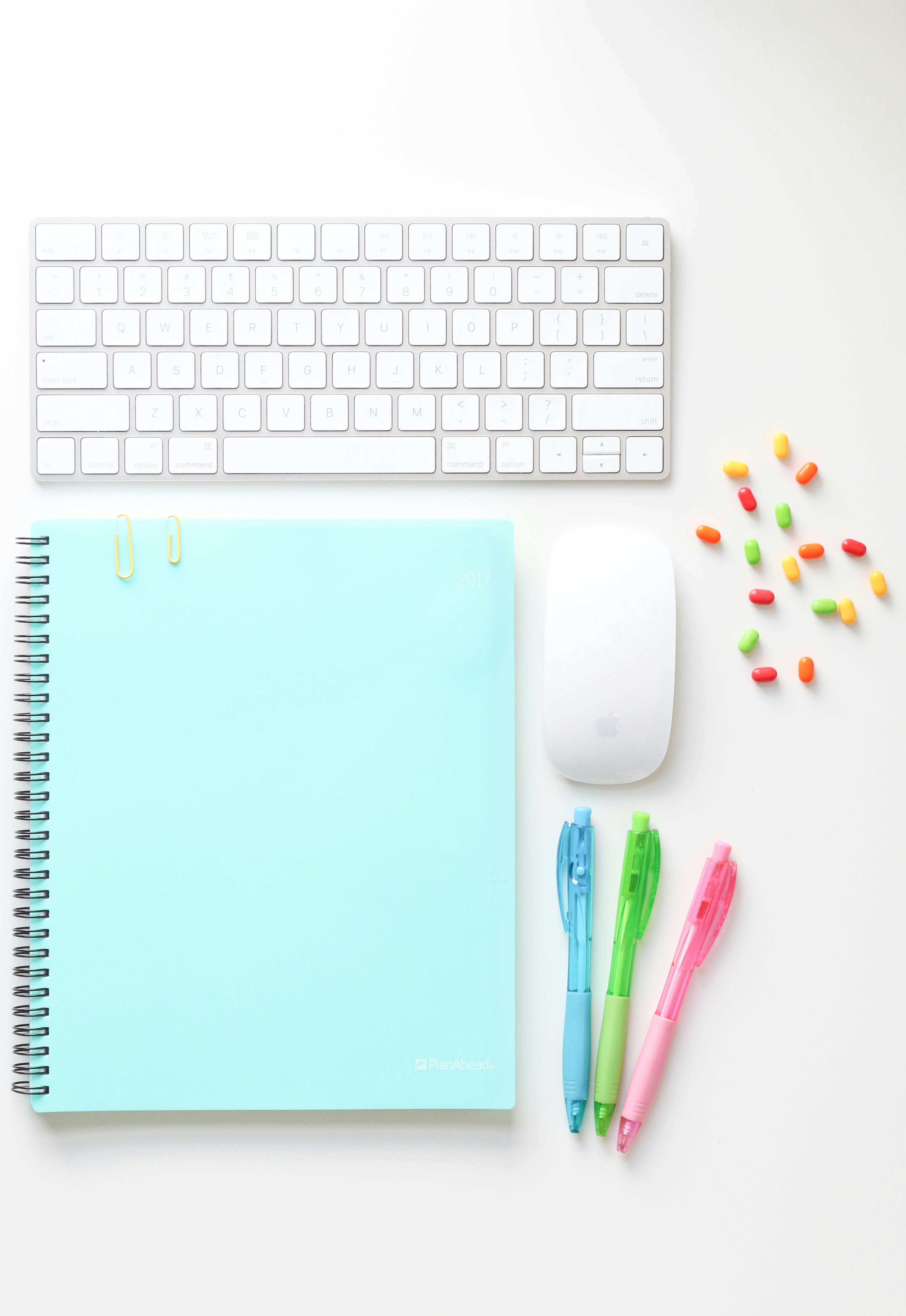 White keyboard, blue notebook, with a green, blue, and pink pen