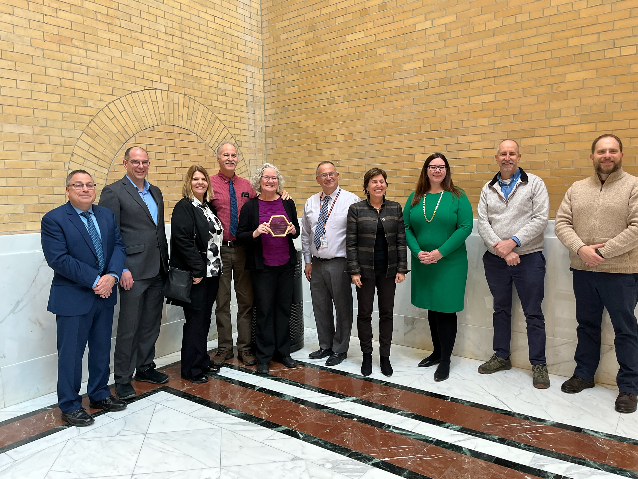 Tara Gallagher, at center holding the Leading By Example award, with DOER Commissioner Elizabeth Mahoney, other state officials and colleagues in Salem State's Sustainability and Environmental Health and Safety division.