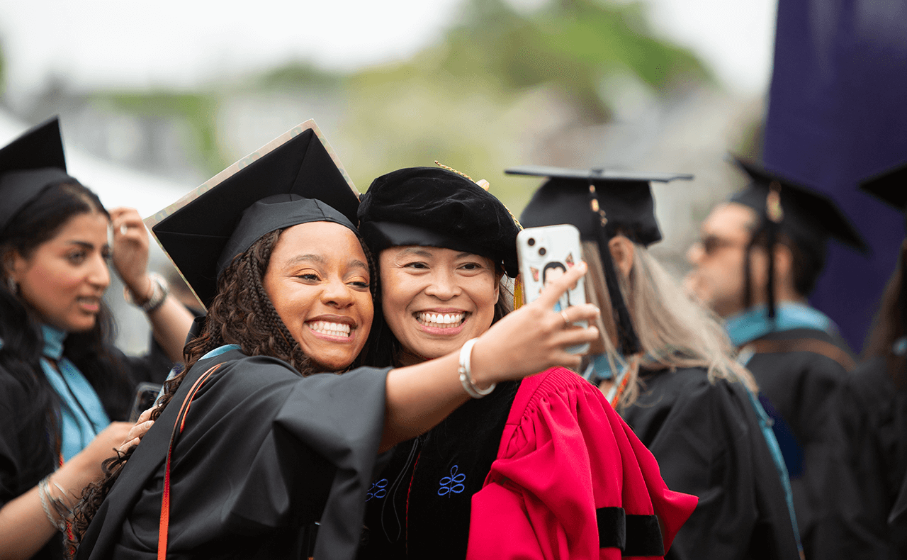 Black Female Graduate Smiling with Asian Female Professor on Commencement Day, taking a Selfie