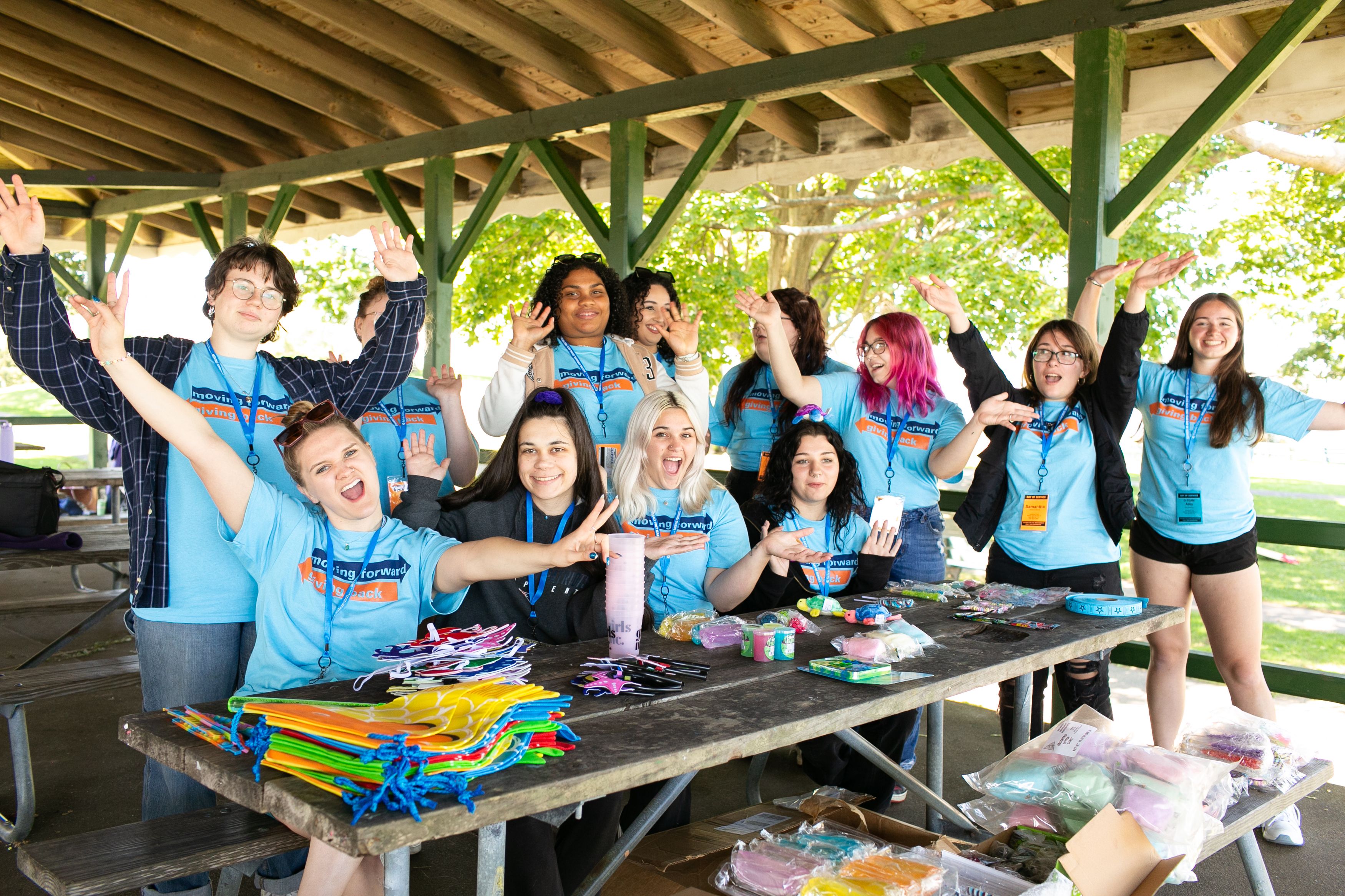 Group of excited students in matching shirts sitting and standing around a picnic table