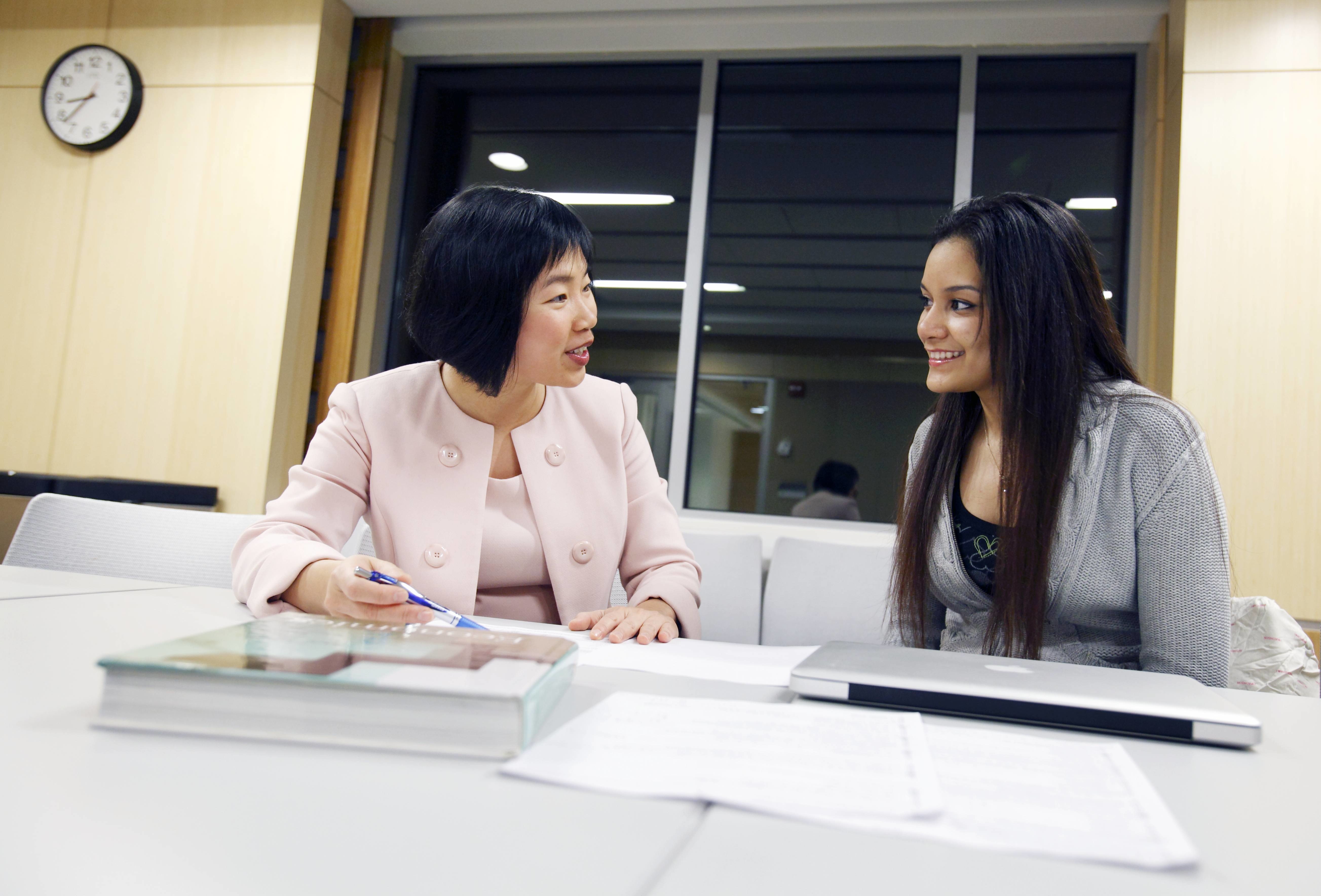 Two professionally dressed women sit together at a table 