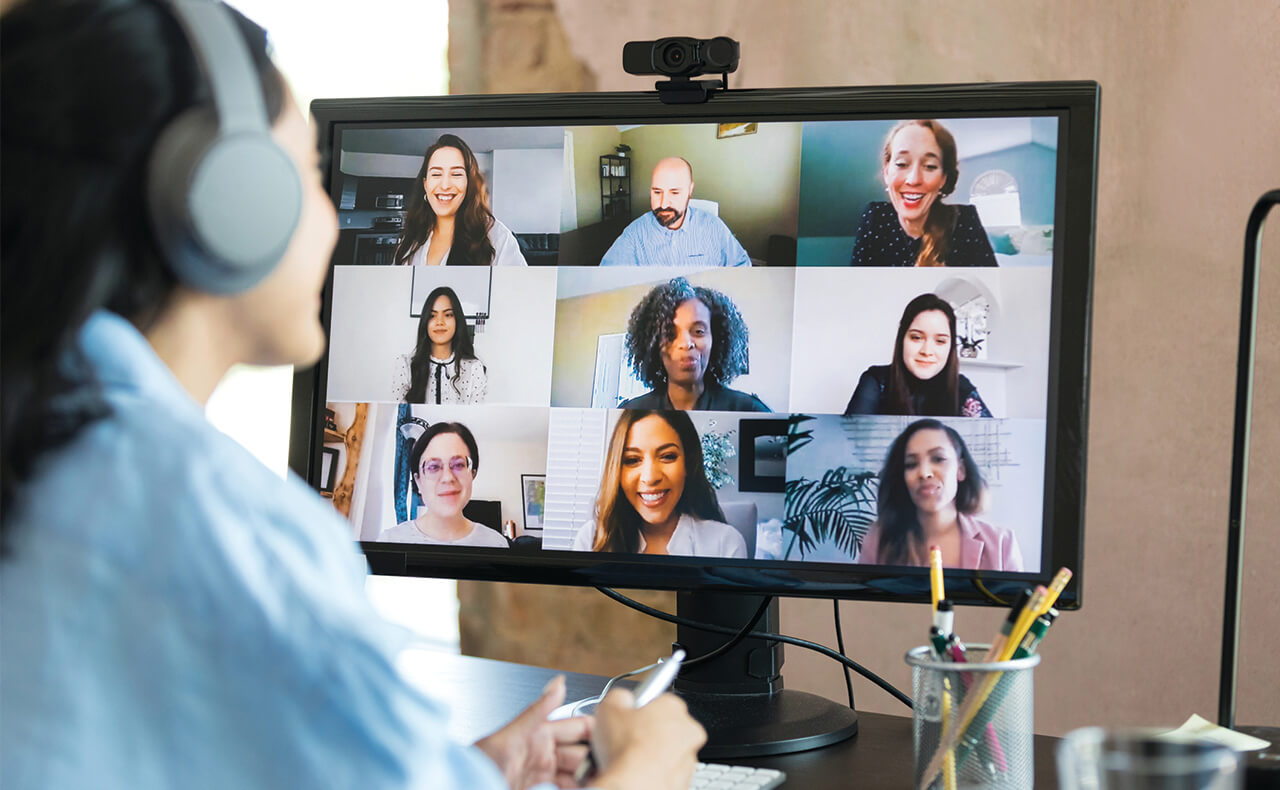 A female student participates in a synchronous course with other students who all appear on the computer monitor, smiling