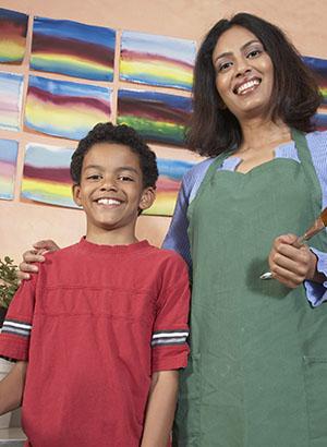 A teacher and her elementary-age student stand in front of classroom artwork