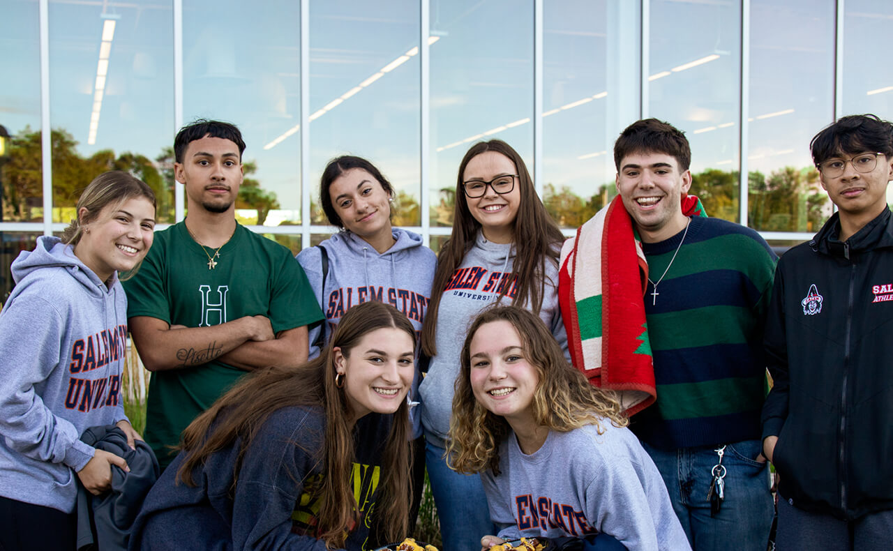 A group of coeds gathered together in front of Gassett Fitness Center celebrating Superfan tailgate, wearing Salem State apparel and smiling