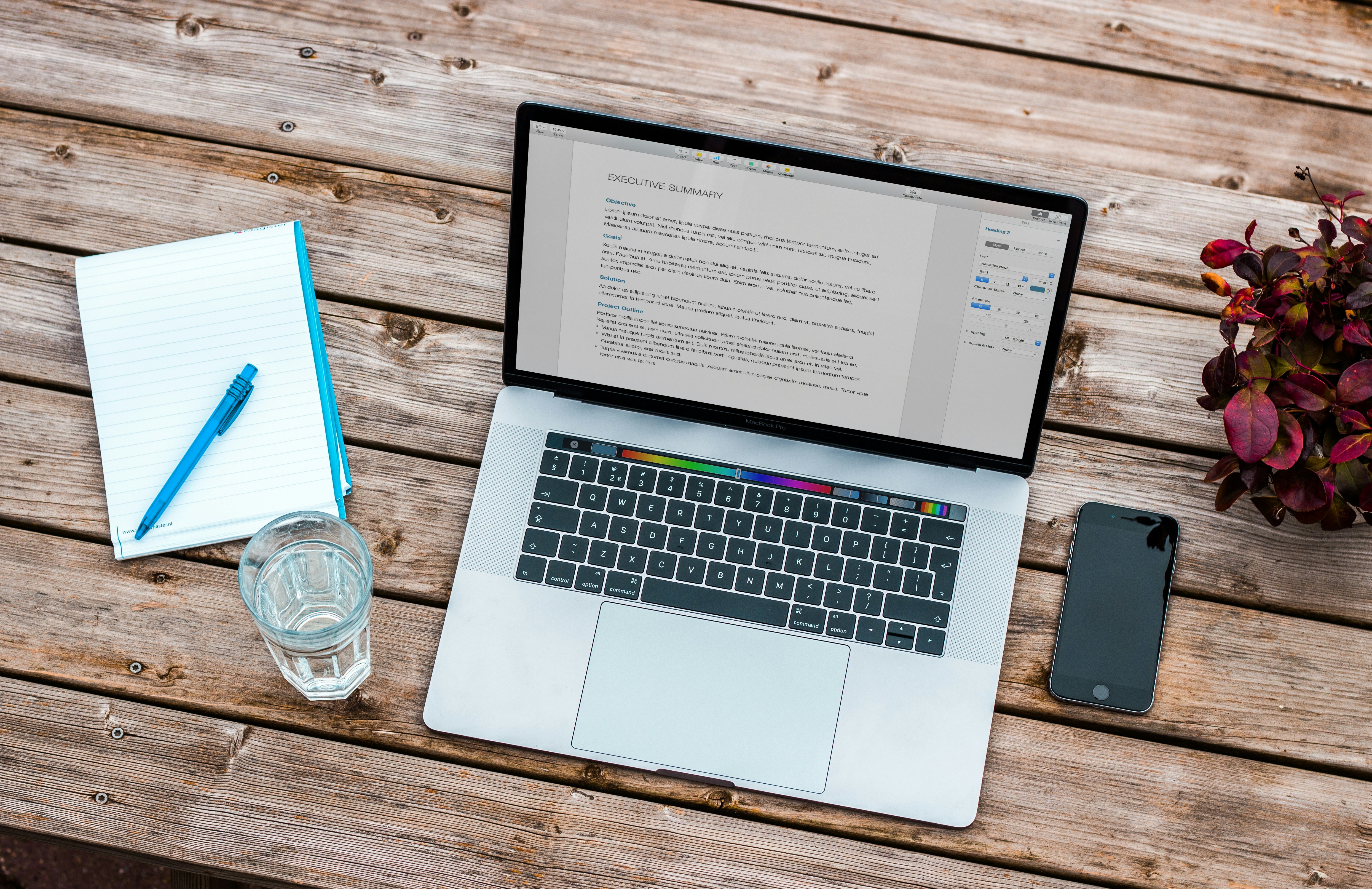 Table with laptop, notepad/pen, cell phone, and glass of water on it.