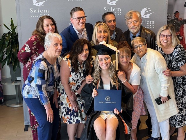 Graduate posed with family and guests in front of Salem State photo backdrop