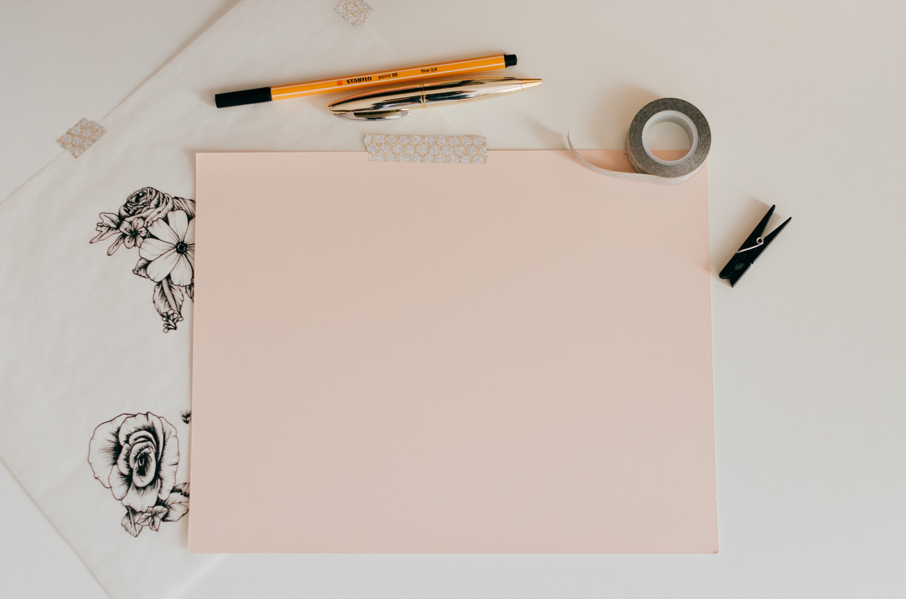 Pieces of light pink paper with scissors, pencils, and pens around it.