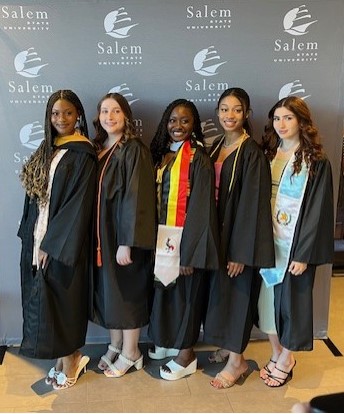 Graduates posed standing together in cap and gown in front of Salem State photo…