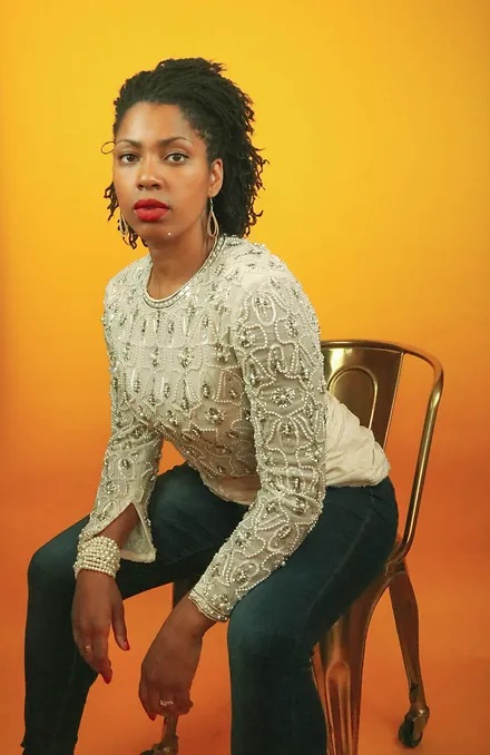 Jenny Oliver sitting on a chair with a gold background