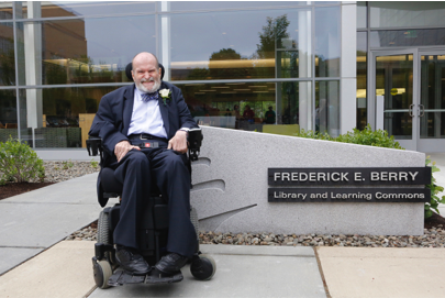 Frederick Berry in wheelchair outside of new library building, positioned in front of sign titled Frederick E. Berry Library and Learning Commons