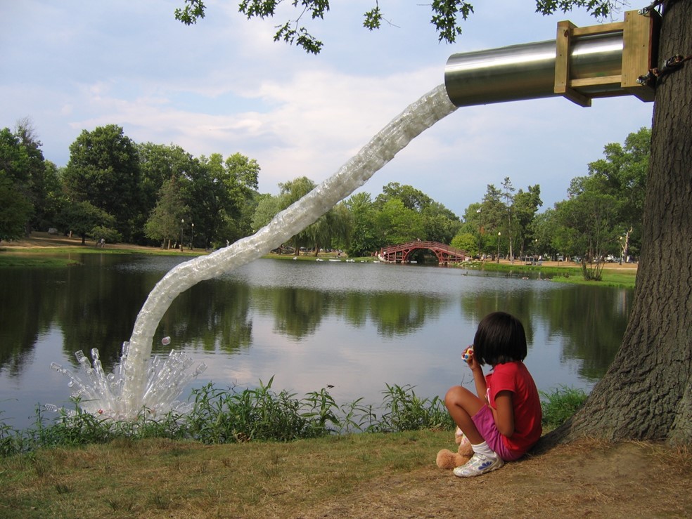 Child squatting in front of a large sculptural faucet with water coming out