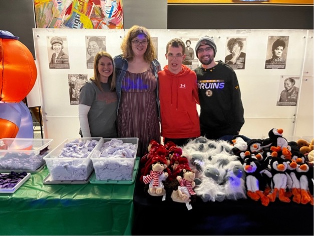 Students and staff stand behind a table covered in stuffed animals.