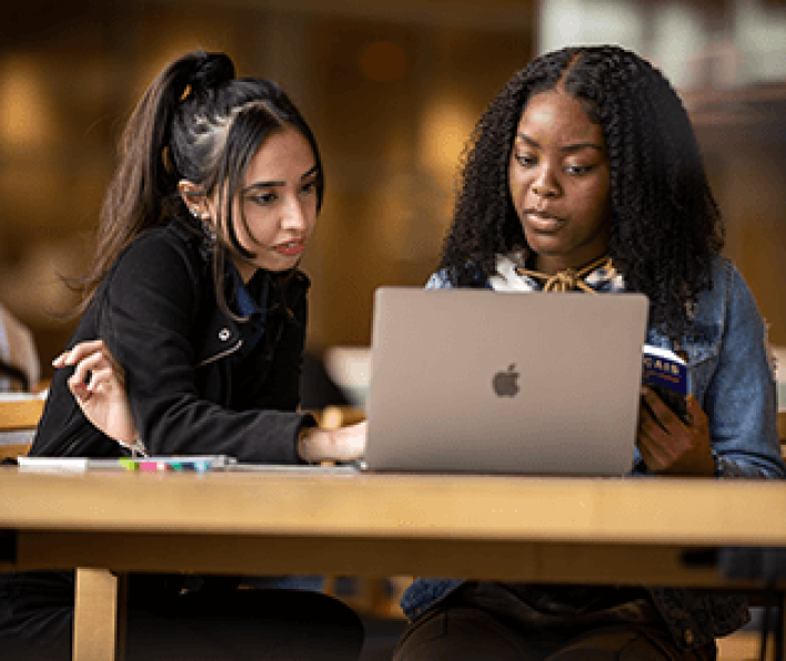 Two diverse female students collaborating on a laptop in the library