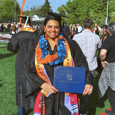 Salem State student Miah Reyes in cap and gown holding diploma outside after Commencement