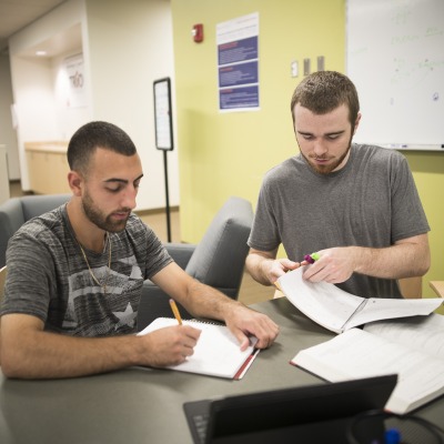 Two male students sit together in the library to study for a paper.