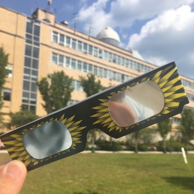 A student holds up a pair of solar eclipse protective glasses in front of Salem State University's Collins Observatory