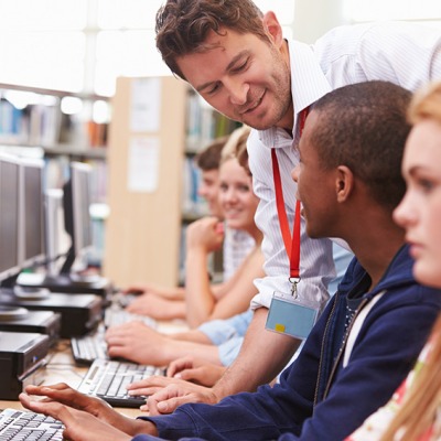 A librarian helps teenage students at computers in a library