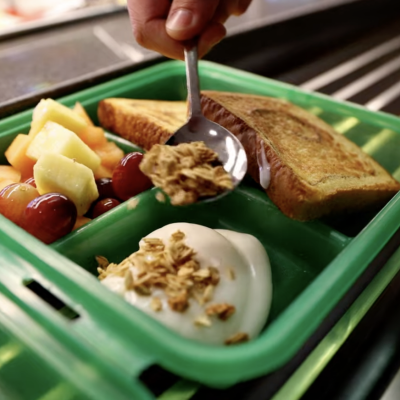A green compostable OZZI container getting filled with breakfast foods.