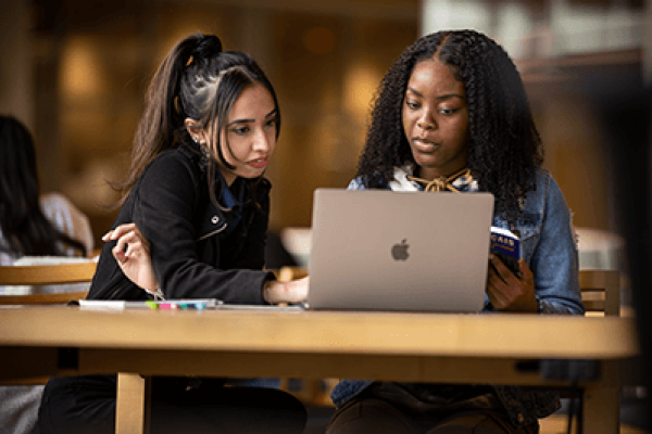 Two diverse female students collaborating on a laptop in the library