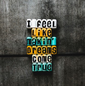 concrete wall background with the words "I feel like makin' dreams come true" in blue white and orange coloring.